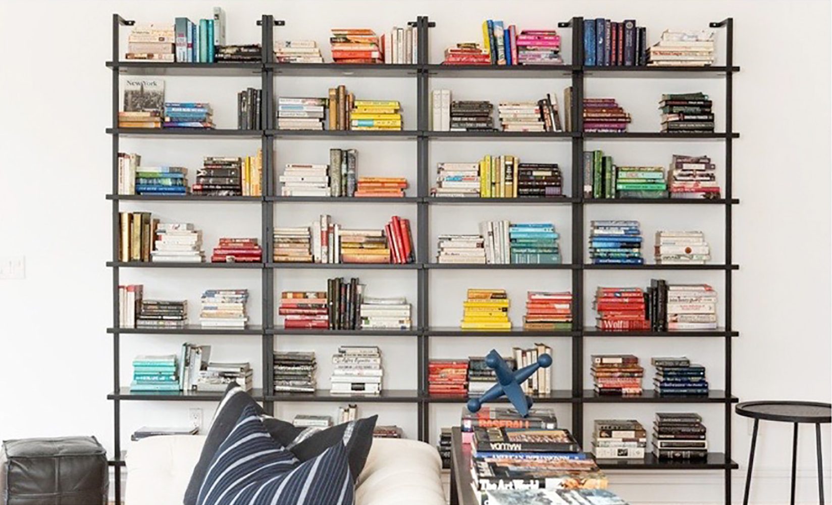 A wall-mounted, minimalist black bookcase styled with books grouped by color.