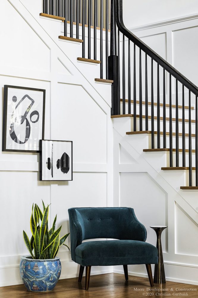 A pair of black and white abstract paintings hung from decorative woodwork beneath stairway.