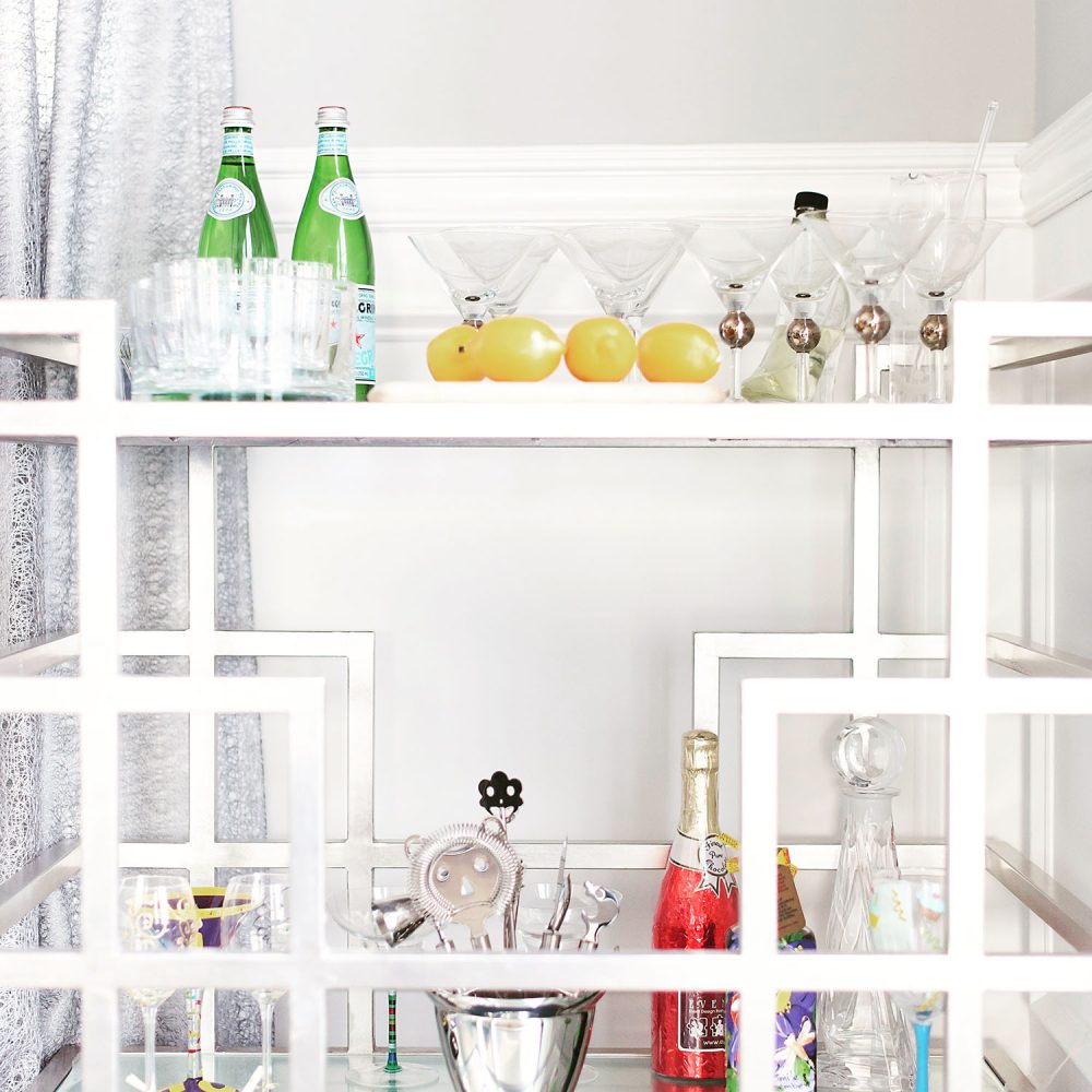 A closeup of a modern, silver bar cart with glassware, bar tools, wine and Pellegrino water.