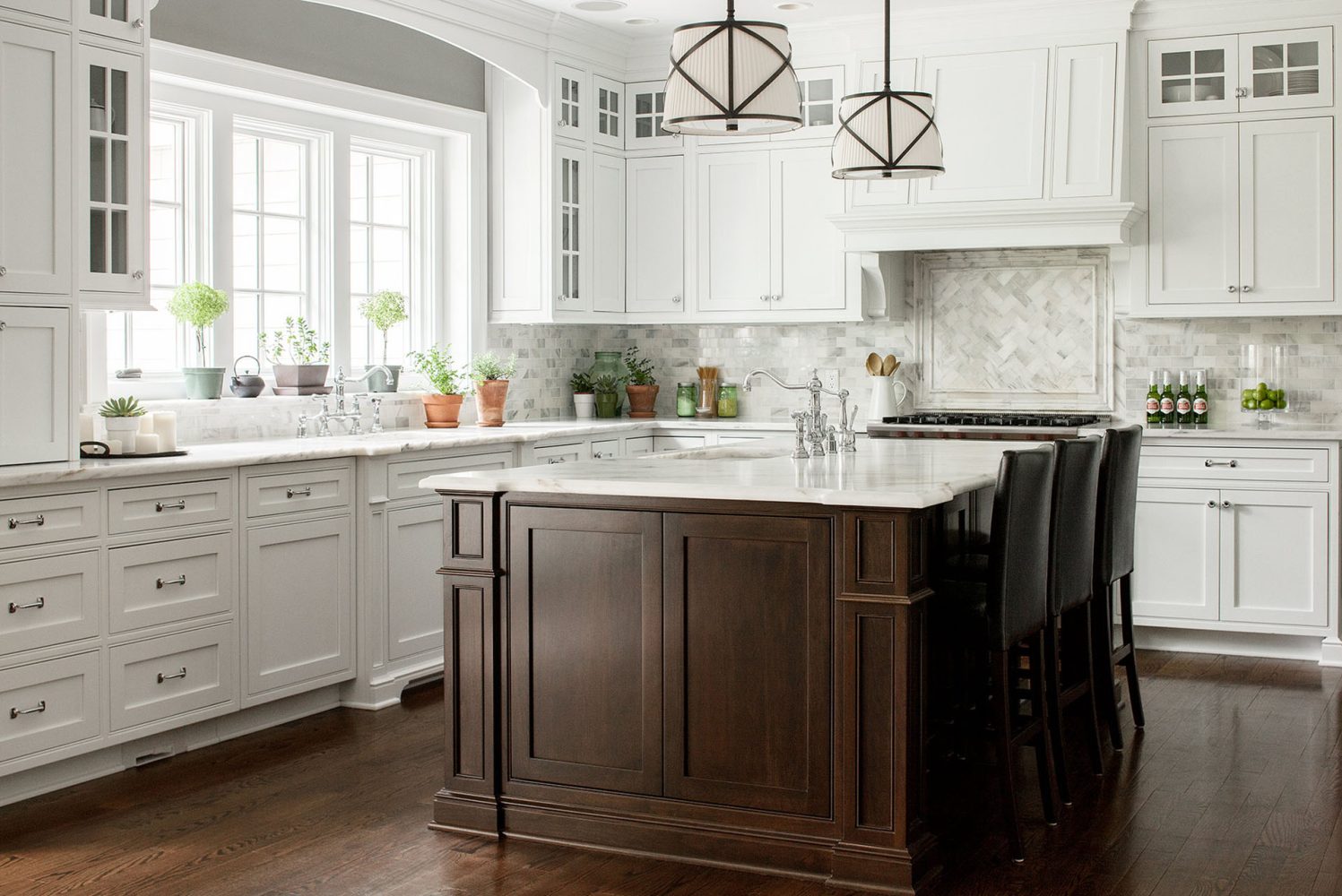 Kitchen with white cabinetry, white marble tile, and a dark brown island with white countertop and sink inset. Pendant lights are white shades with decorative metal overlay.